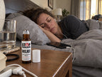 Woman resting in bed with earbuds, STOP MIGRAINE RELIEF roll-on on the nightstand